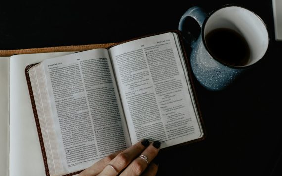 person reading book beside white ceramic mug with coffee